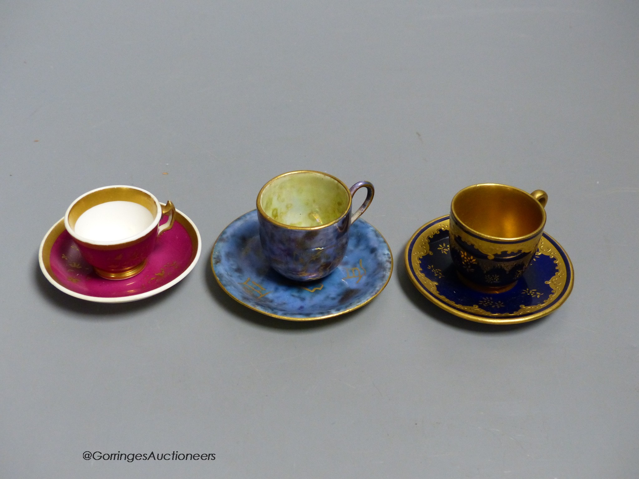 A Wedgwood lustre miniature cup and saucer with gilt decoration, a Coalport blue and raised gilt cup and saucer and a Grainger Worcester claret ground miniature teacup and saucer, tallest 3.5cm including saucer